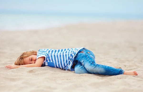 Втомився, але щасливий молодий хлопчик лежить на піщаному пляжі після виснажливих розважальних ігор — стокове фото