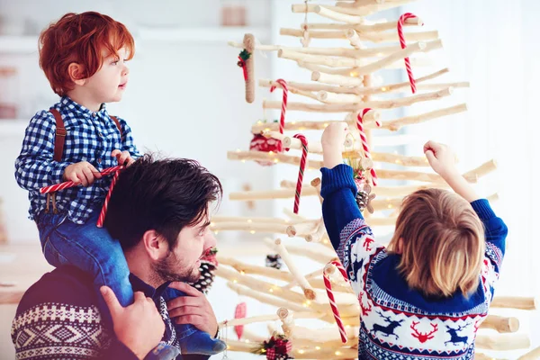 Lycklig familj dekorerar en extraordinär julgran gjord av grenar och drivved hemma — Stockfoto