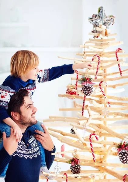 Lycklig far och son dekorera en extraordinär julgran gjord av grenar och drivved hemma — Stockfoto