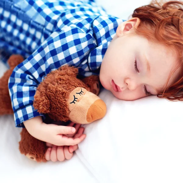 Adorável ruiva criança bebê dormindo com brinquedo de pelúcia em pijama de flanela — Fotografia de Stock