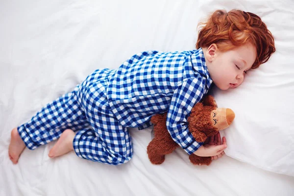Entzückendes rothaariges Kleinkind schläft mit Plüschtier im Flanell-Pyjama — Stockfoto