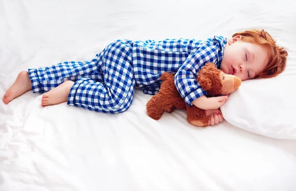 Entzückendes rothaariges Kleinkind im Flanell-Pyjama, das mit Plüschwärmer schläft — Stockfoto