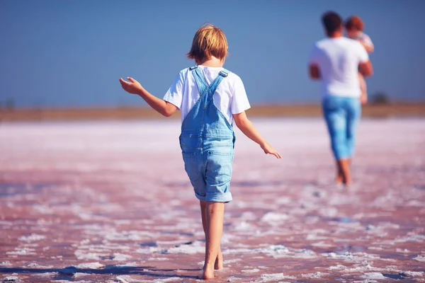 Chico joven en jeans romperse caminando a través del lago de sal rosa, firth —  Fotos de Stock