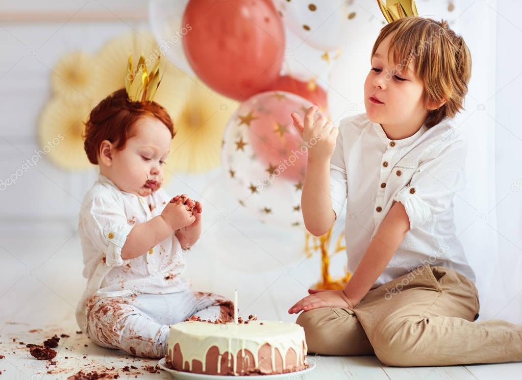 cute kids, brothers tasting birthday cake on 1st birthday party