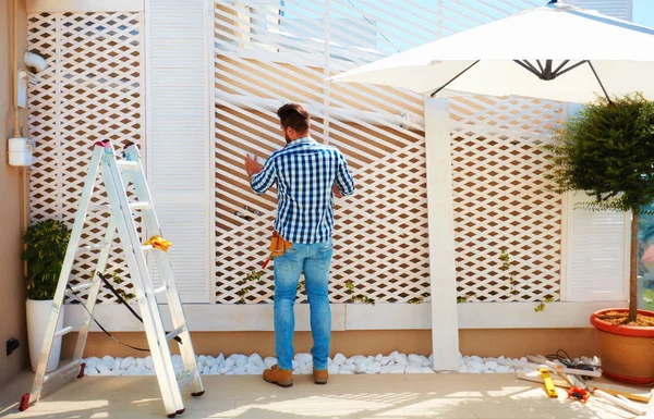 Hombre adulto joven construyendo la pared de pérgola de madera en la zona del patio de la azotea —  Fotos de Stock