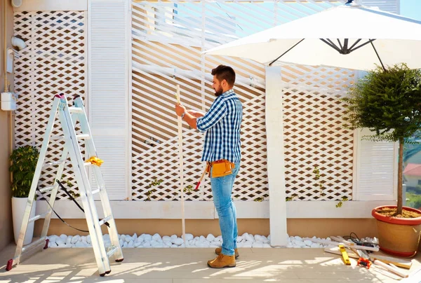 Junger erwachsener Mann baut hölzerne Pergola-Wand auf Dachterrasse — Stockfoto