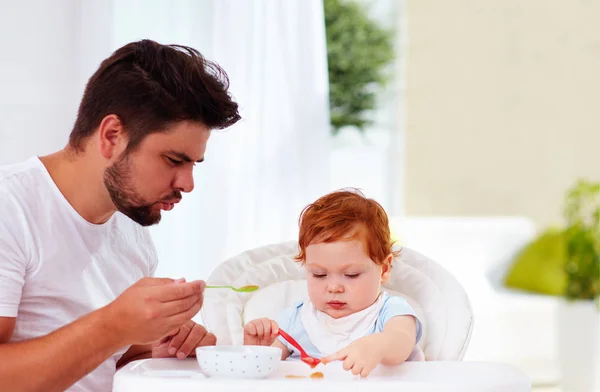father teaches son, baby to hold the spoon and eat by his own