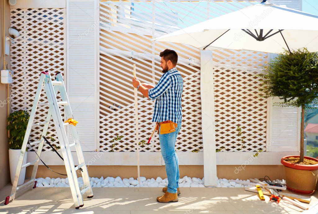young adult man building wooden pergola wall on rooftop patio zone