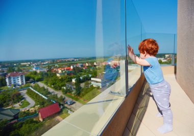 infant baby boy enjoying the city view from the rooftop patio at multi storey building clipart