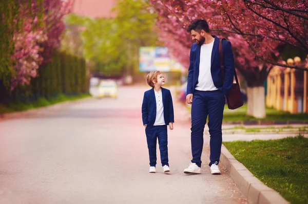 Pai feliz e filho andando juntos ao longo florescendo rua primavera, vestindo ternos — Fotografia de Stock