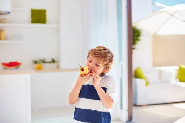 Cute kid, young boy eating tasty cupcake with whipped cream and fruits at home — Stock Photo, Image