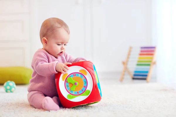 Χαριτωμένο μικρό μωρό κορίτσι που κάθεται στο χαλί μεταξύ τα πολύχρωμα παιχνίδια — Φωτογραφία Αρχείου