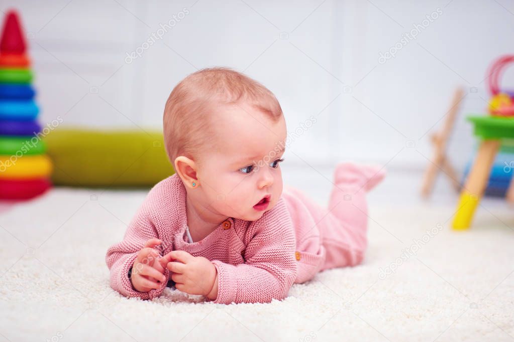 cute little baby girl crawling on the carpet among the development toys