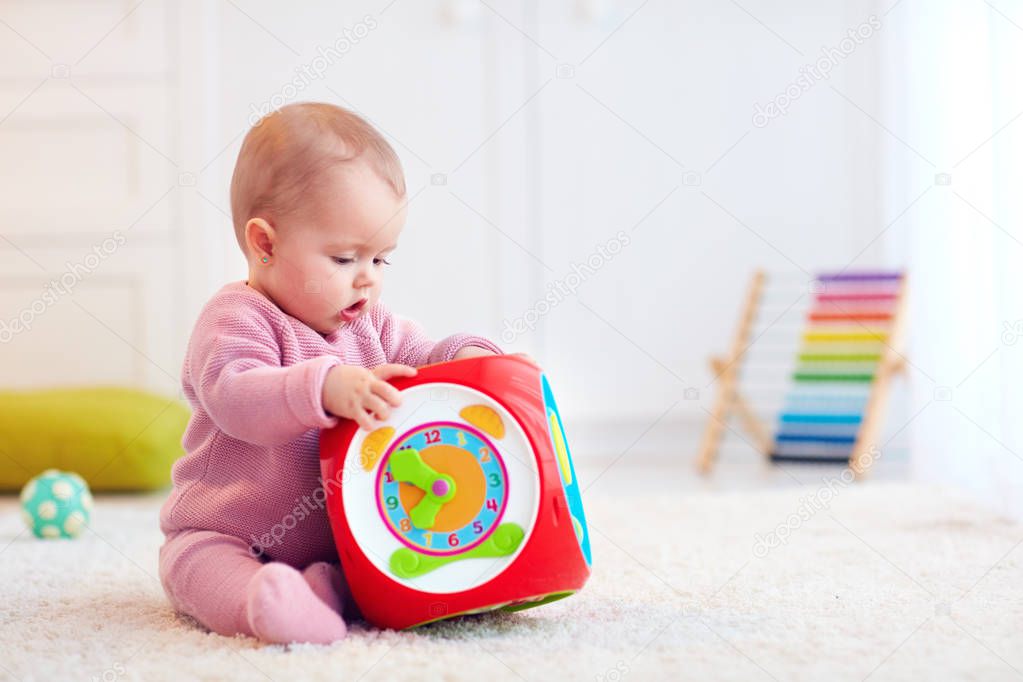 cute little baby girl sitting on the carpet among the colorful toys