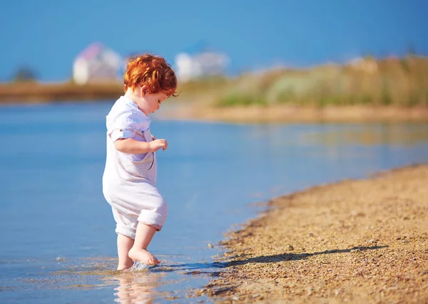 Cute redhead toddler baby boy walking in water at summer lake coast — Stock Photo, Image