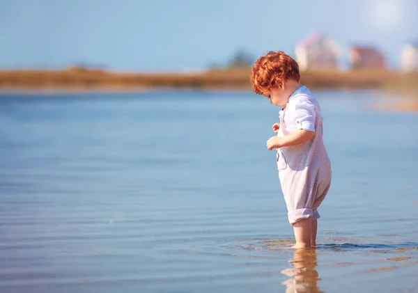 Cute redhead toddler baby boy standing in water at summer lake coast — Stock Photo, Image