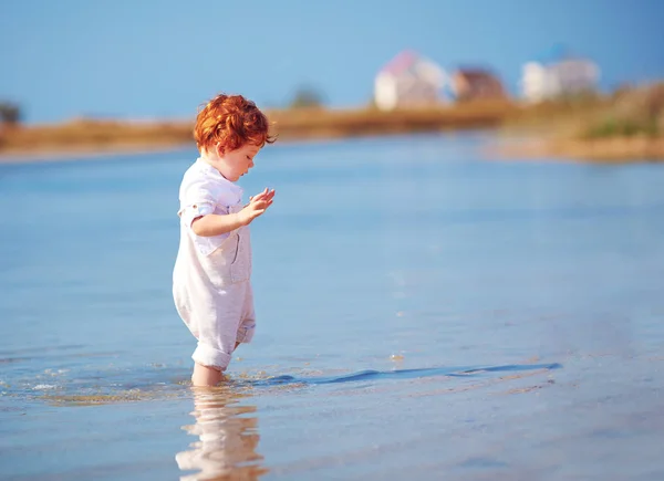 Cute redhead toddler baby boy walking in water at summer lake coast — Stock Photo, Image