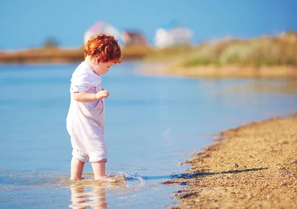 Carino rossa bambino bambino a piedi in acqua a estate costa del lago — Foto Stock