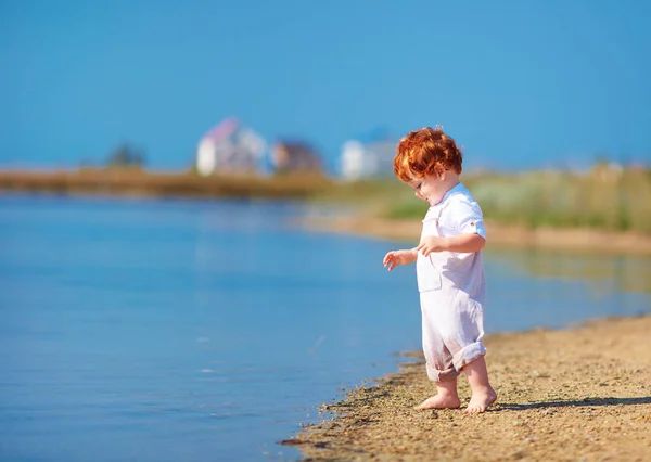 Roztomilá zrzka batole chlapeček chůzi na pobřeží jezera v letní ráno — Stock fotografie