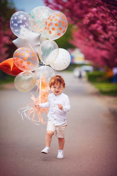 Menino criança feliz correndo a rua primavera com o bando de balões de ar — Fotografia de Stock