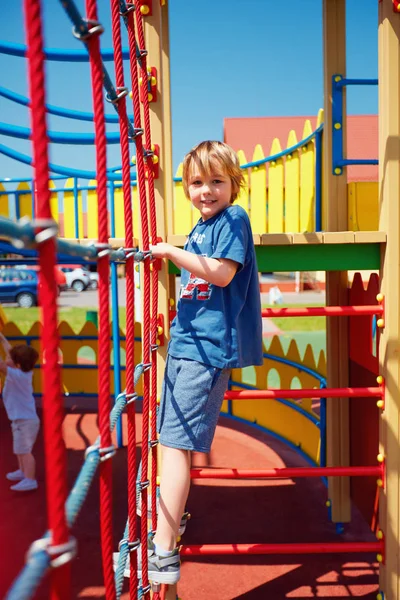 Счастливый ребенок лезет по веревочной стене, играя в игры на красочной игровой площадке замка — стоковое фото