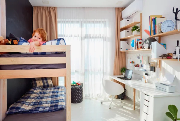 Niño feliz se encuentra en el nivel superior de la litera en la habitación de los niños brillantes — Foto de Stock