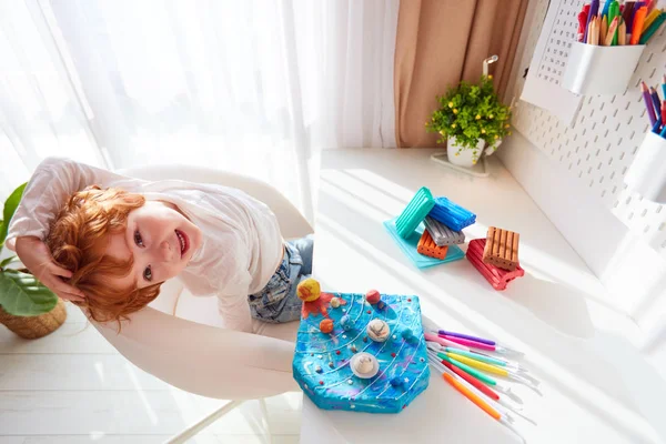 Niño feliz sentado en el escritorio con el sistema solar hecho a mano, hecho de plastilina de modelado —  Fotos de Stock