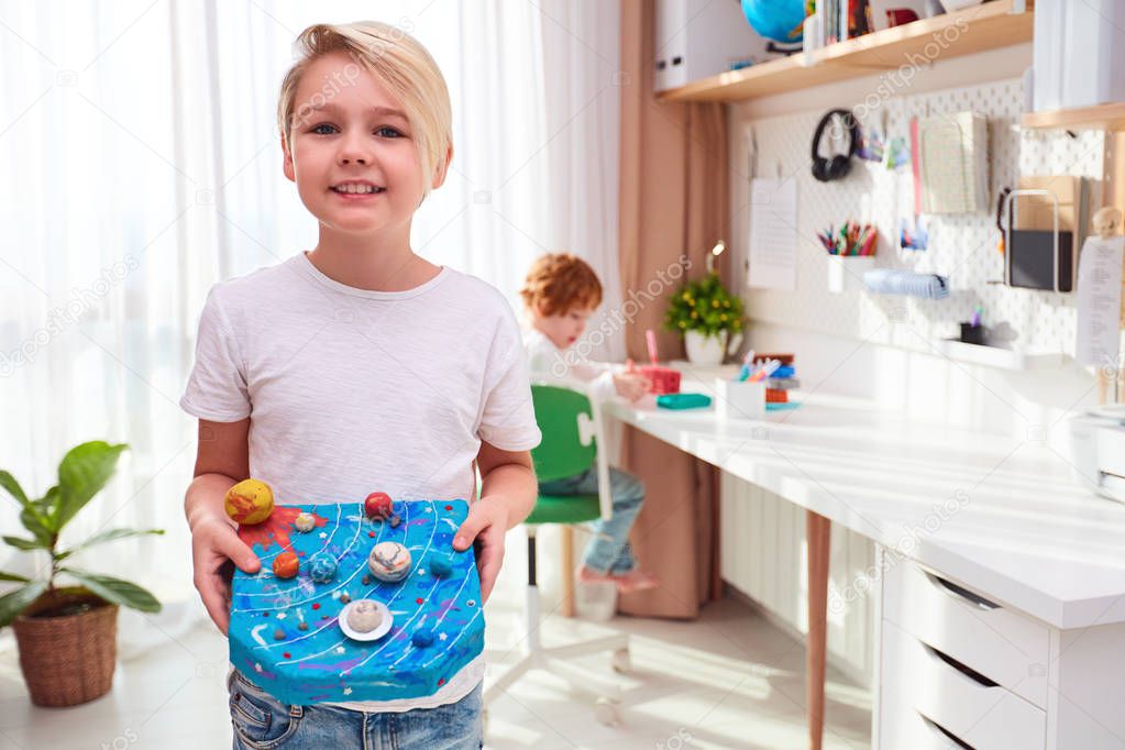 happy young school kid, boy showing the model of solar system made from plasticine, kids room background