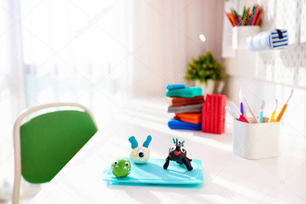 cute creatures, hand crafts made of plasticine by kids, on the desk in the kids room