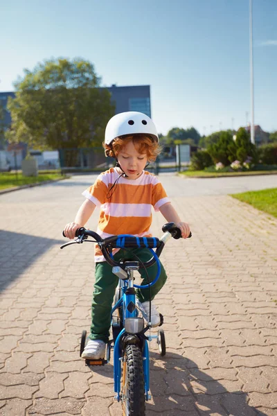 Tatlı kızıl çocuk, çocuk mahallede üç tekerlekli bisiklet sürüyor. — Stok fotoğraf