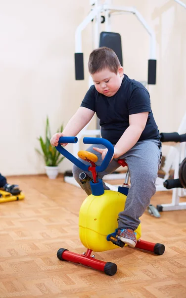 Lindo Niño Con Síndrome Haciendo Ejercicio Bicicleta Estacionaria Centro Deportivo — Foto de Stock