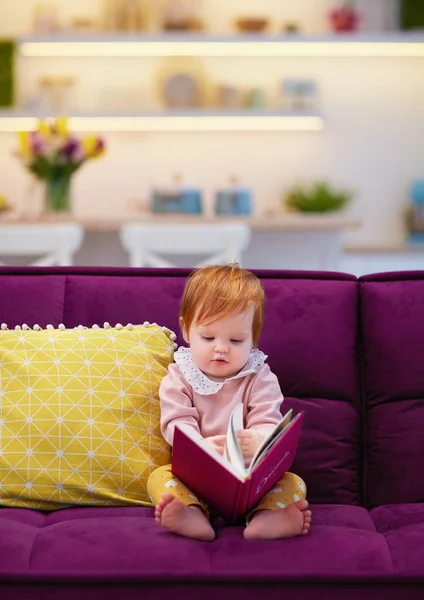 可爱的蹒跚学步的小女孩翻着书 坐在客厅的沙发上 — 图库照片