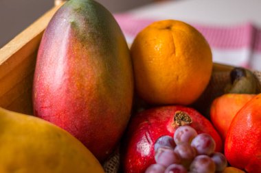 Tahta sepetteki meyveler: kaju, portakal, üzüm, muz, mango ve papaya