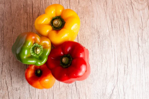 Some red, green and yellow bell peppers over a wooden surface.