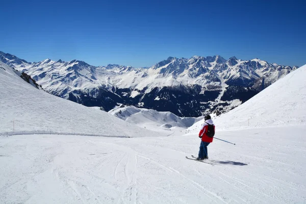 晴れた日に背景に高い山脈を背景に広いオープンスキー場でスキーをする人 — ストック写真