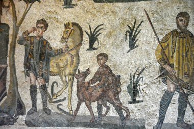 Bir av sahnesinin antik Roma Mozaiği. Avcı iki çatallı mızrağını tutuyor. Bir çocuk bir Sighthound (vertragus) tutuyor. Sicilya, Villa Romana del Casale 'deki Little Hunt sahnesinden.