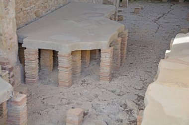 Mozaik zeminin altında hipokost ısıtma adı verilen eski Roma merkezi ısıtma sistemi. UNESCO 'da Sicilya' daki Villa Romana del Casale 'deki Antik Roma mozaikleri listelendi.