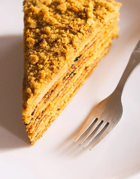 Close up sweet home layered honey cake with sun-dried prunes on a white plate with a silver fork