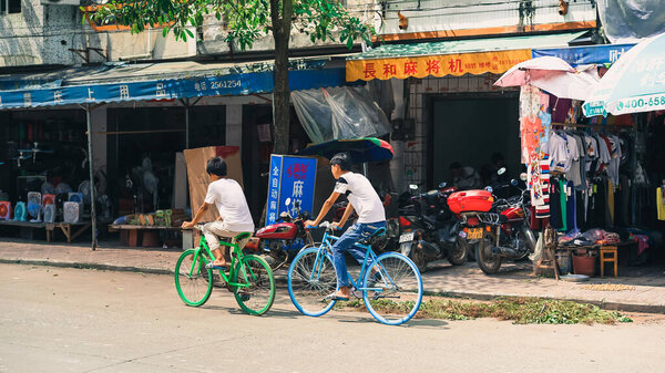 Yingde, China - July 16, 2016: a street of a typical small urban city in China, daytime, hot weather, no crowds, empty street in Asia, a couple of friends cycling bicycle for shopping