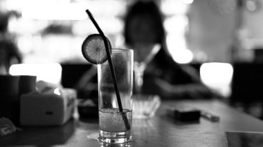 Barda siyah pipet ve limon dilimli soda kokteyli, bir barda yarı sarhoş alkol içeceği, restoran, tahıl film efekti, bir barda yarı boş bardakta içki, siyah-beyaz.