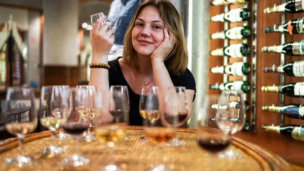 Blurred closed up view beautiful happy Caucasian girl is drinking a glass of white wine, film noise, tasting alcoholic drinks concept, glasses of champagne, portwein and red wine on the  wooden table