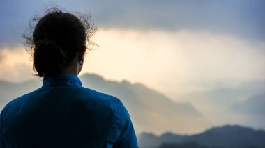 Seçici odak noktası, mavi rüzgarsız ceketli genç bir kız dağların üzerinden gün doğumunu seyrediyor, seyahat konsepti, ulusal parkın zirvesine tırmanıyor, yürüyüş ve yürüyüş macerası yaşıyor.