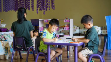 Masanın altında oturan ve Asya özel anaokulunda resim yapan iki küçük Çinli çocuk, çocukların gelişimi için aktiviteler, mutlu bir çocukluk dönemi, anaokulu eğitimi.