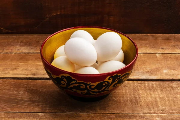 Chicken eggs lie in a wooden bowl. A bowl stands on a wooden background.