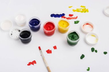 Beyaz arka planda bir kavanoz dolusu guaj boyası. Sanatçı kağıdın üzerindeki boyanın rengini deniyor.