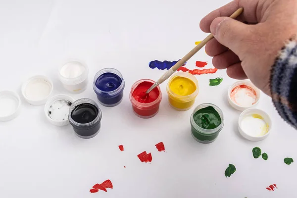 Open jars of gouache paint on a white background. The artist tries the color of paint on paper.