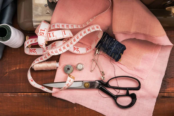 Sewing tools lie on pink fabric. Needles, threads and scissors are prepared for the job.
