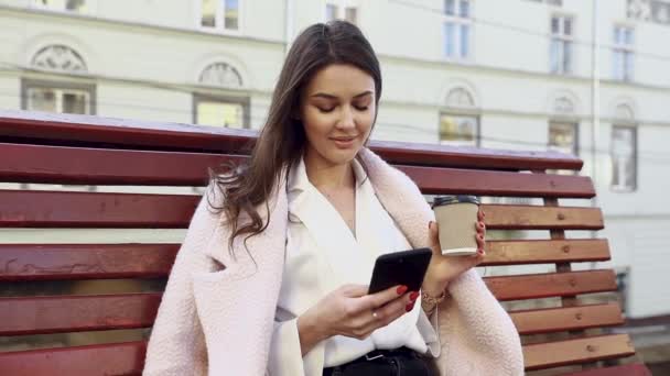 Красивая Европейская Девушка Сидящая Скамейке Пользующаяся Телефоном Кофе Руке Портрет — стоковое видео