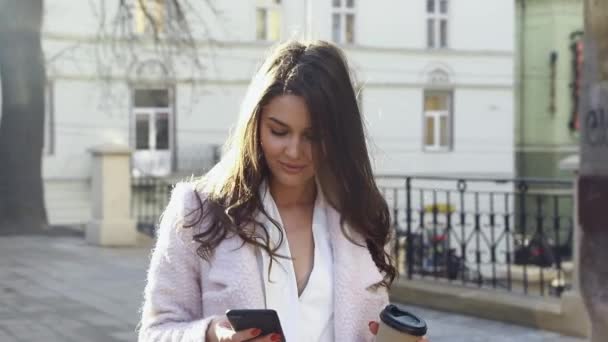 一个迷人的女人站在街上用她的智能手机打字 玩的开心 在户外享受时光 漂亮的黑发 智能手机在相机前 漂亮的女孩 — 图库视频影像