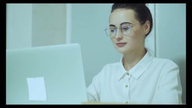 Güzel ve yaratıcı genç kadın oturma onu masa kullanarak laptop bilgisayar. Arka plan parlak ofiste genç profesyoneller çeşitli takım çalışma